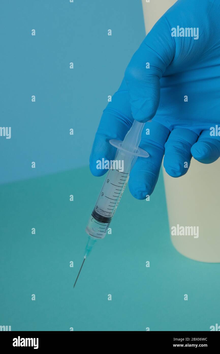 seringue d'injection medical.injection. Concept de vaccination.seringue dans une main dans un gant médical sur fond bleu, vert, jaune. Banque D'Images