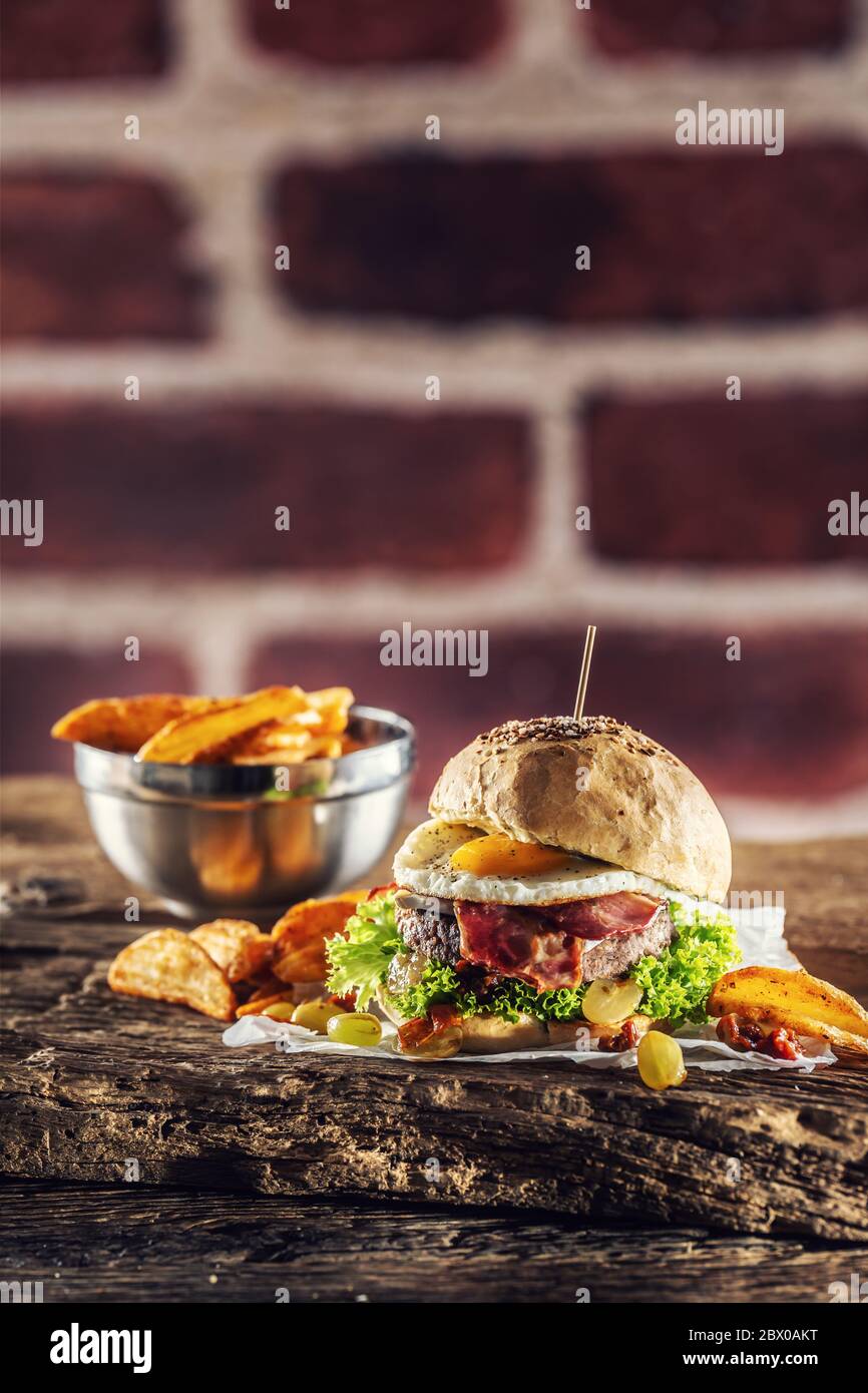 Hamburger de bœuf avec œuf frit, bacon, laitue, quartiers de pommes de terre et raisins sur un bois rustique Banque D'Images