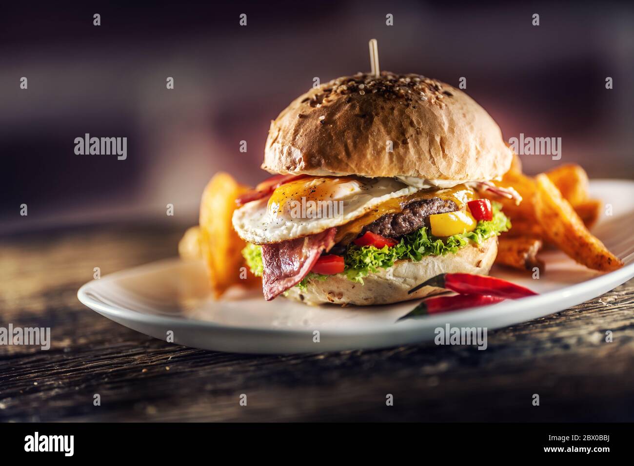 Hamburger de bœuf avec œuf frit, bacon, fromage, laitue et poivrons dans un pain au sésame avec des quartiers de pommes de terre avec paprika fumé et un piment extra frais sur le Banque D'Images