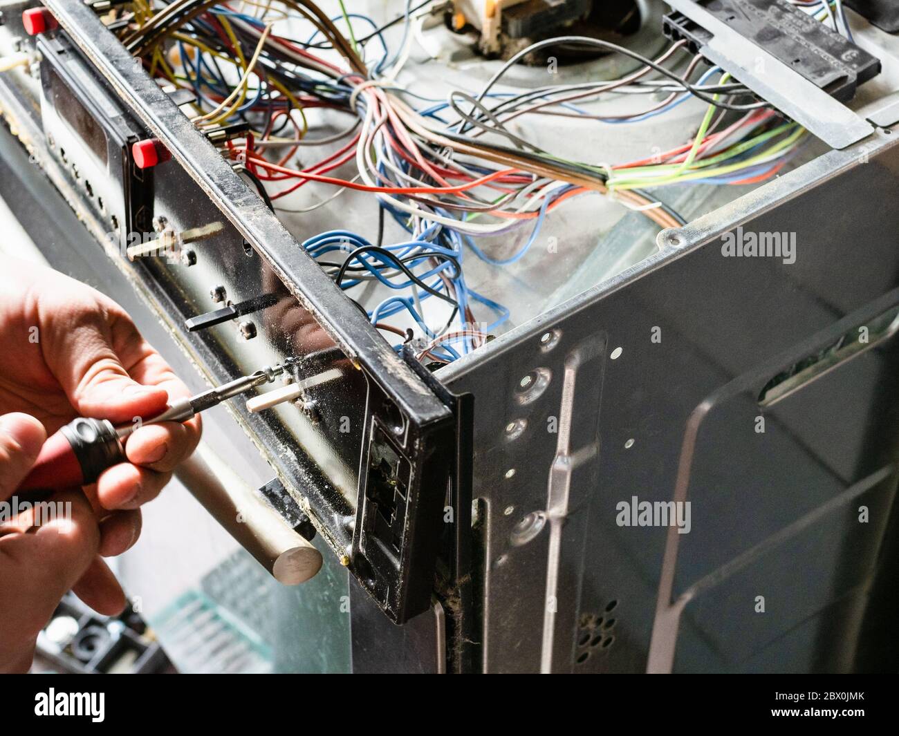 le réparateur fixe le panneau de l'ancien poêle électrique pendant la réparation dans la cuisine maison Banque D'Images