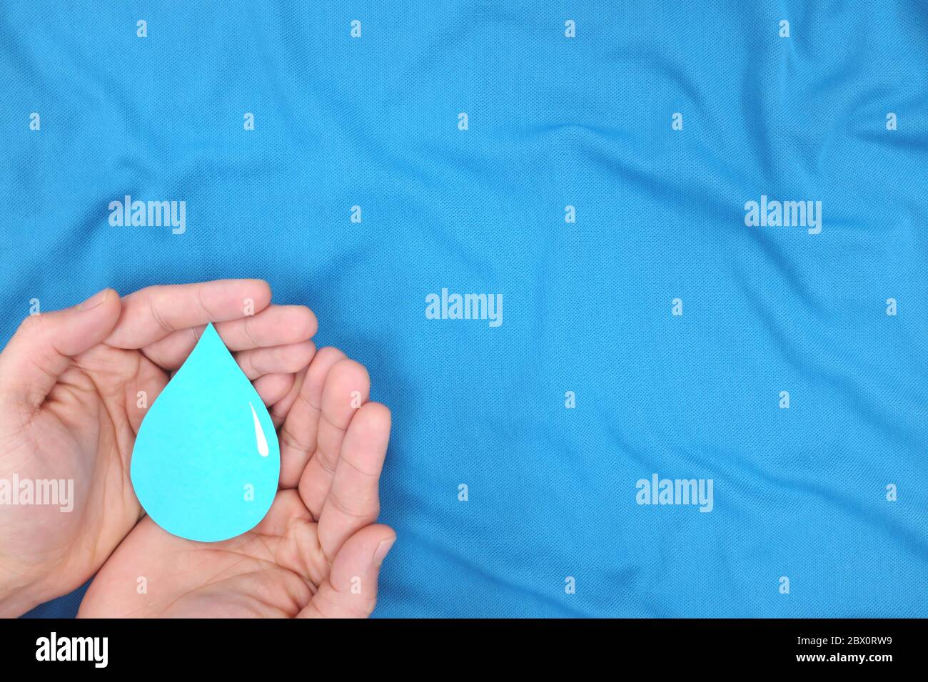 Mains de sexe masculin tenant une goutte d'eau bleue sur fond bleu. Laver les mains, csr, économiser l'eau et concept de la journée mondiale des océans. Vue de dessus avec espace de copie. Banque D'Images