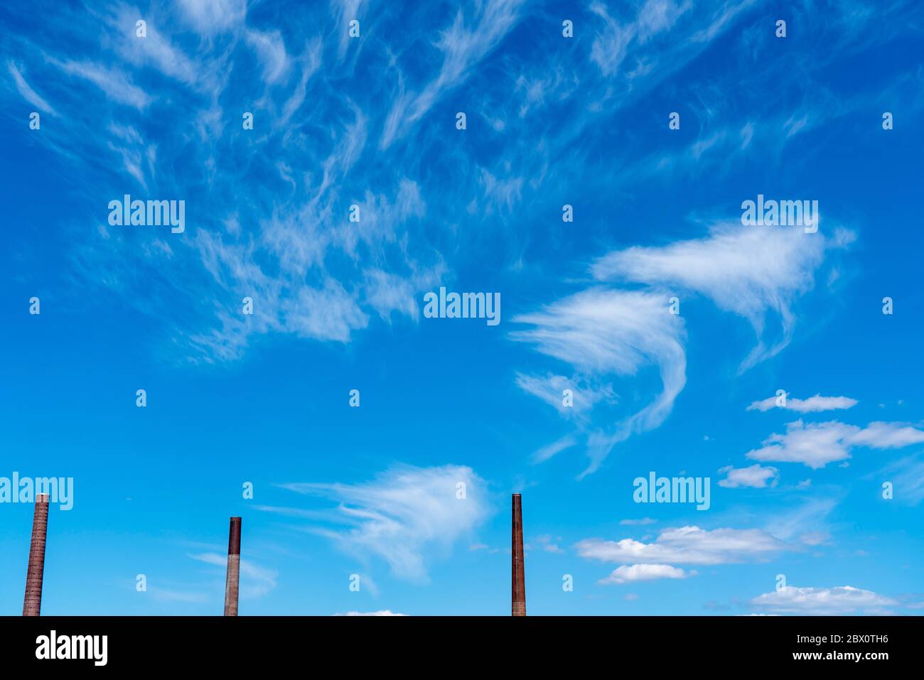 Ciel bleu avec des nuages cirrus, nuages de glace en filigrane à haute altitude, annonciateurs de temps plus chaud, cheminées, émissions Banque D'Images