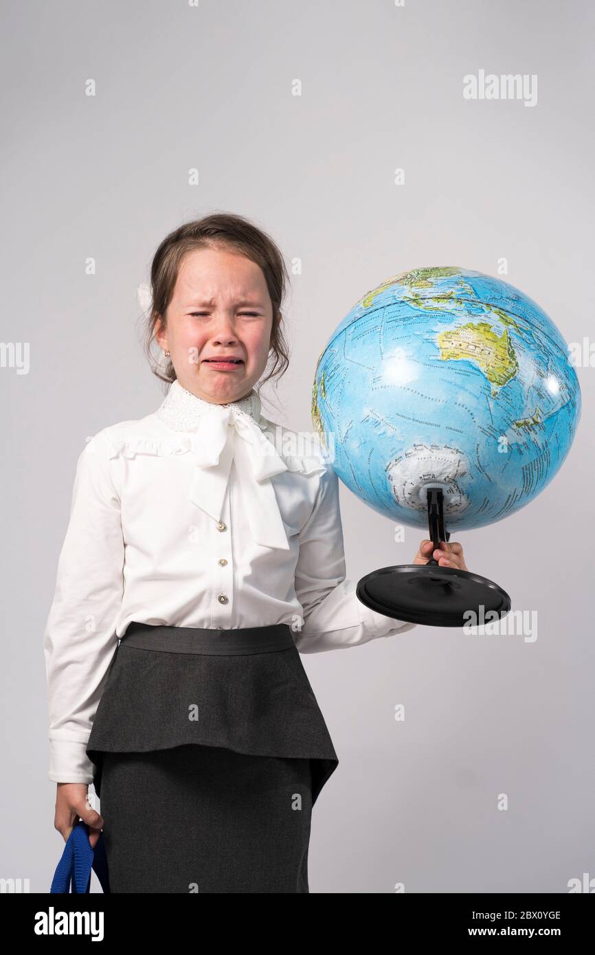 la première école fille dans une chemise blanche tient un globe entre ses mains et pleure Banque D'Images