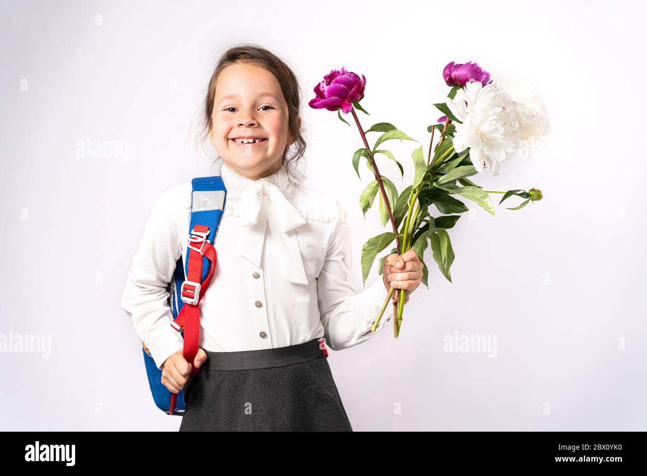 fille d'école de première année dans une chemise blanche tenant des fleurs et un sac à dos Banque D'Images