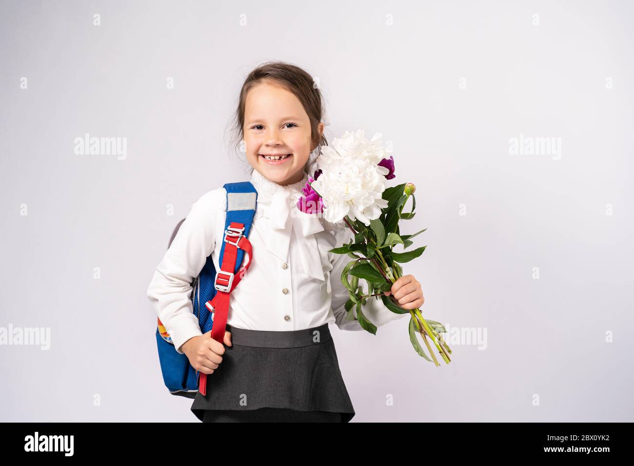 fille d'école de première année dans une chemise blanche tenant des fleurs et un sac à dos Banque D'Images