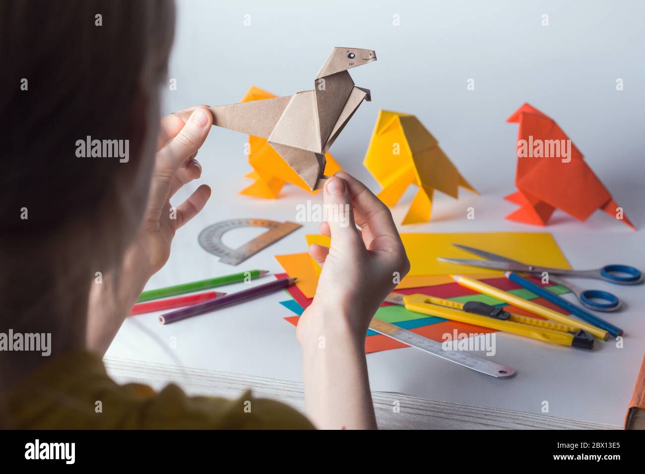 fille fait origami dinosaure de papier de couleur. papier, règle, crayons, couteau. passe-temps intéressant Banque D'Images