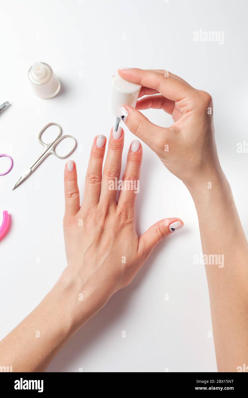 Les mains de femmes peignent les ongles, à côté des dispositifs de pose  pour le soin des ongles. La jeune fille fait une manucure sur fond blanc.  Vue de dessus. Photo de