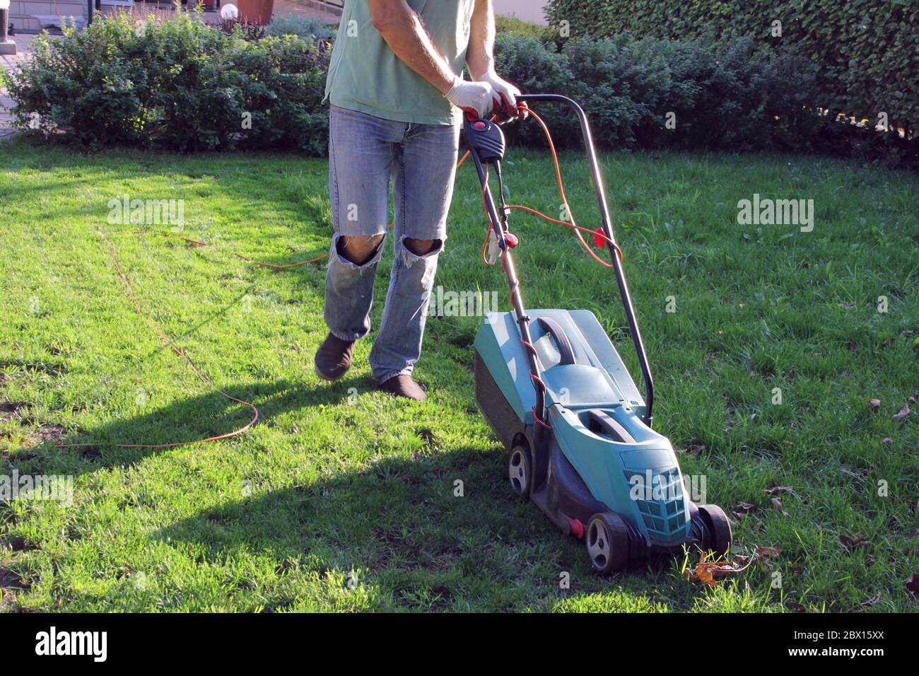 L'homme caucasien tond de l'herbe sur une pelouse avec une tondeuse électrique verte, processus de tonte de la pelouse avec une tondeuse électrique Banque D'Images