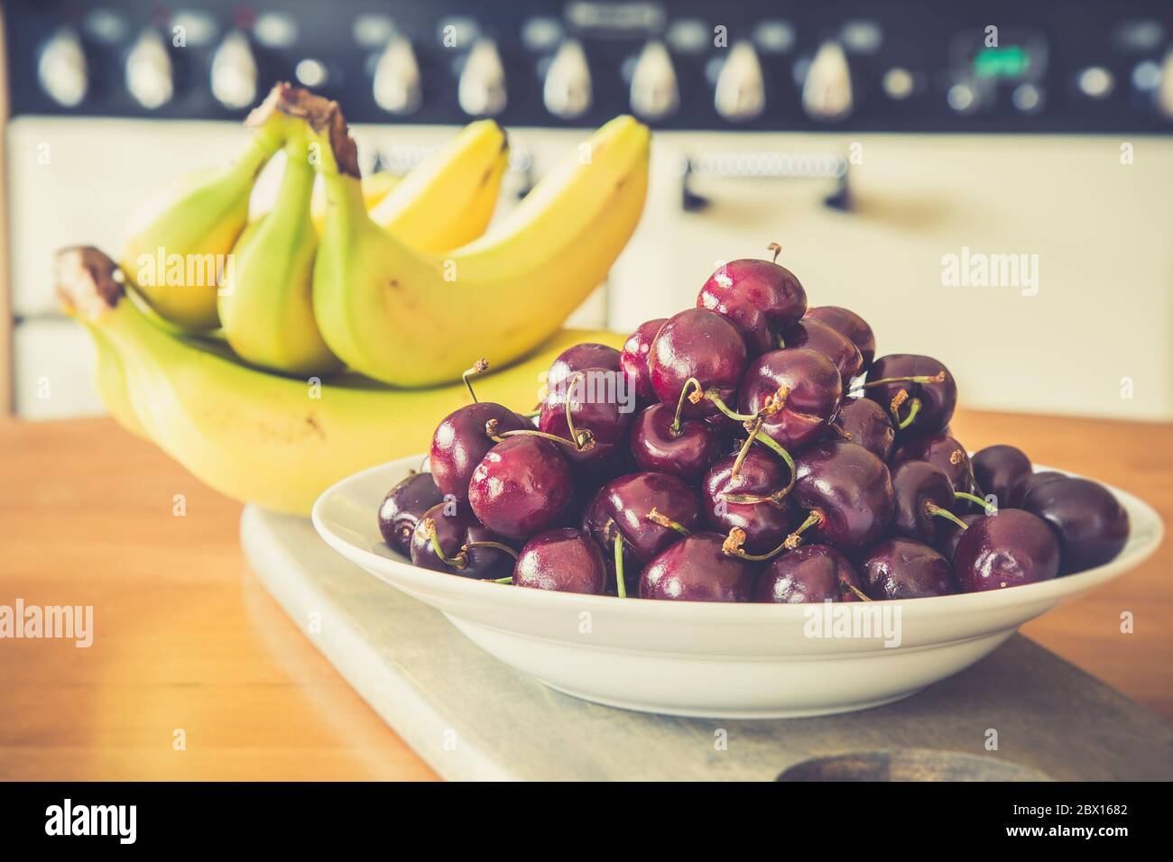 Bol de cerises rouges et bouquet de bananes à l'intérieur sur une table de cuisine britannique en bois. Fruits frais. La vie n'est qu'un bol de cerises. Banque D'Images