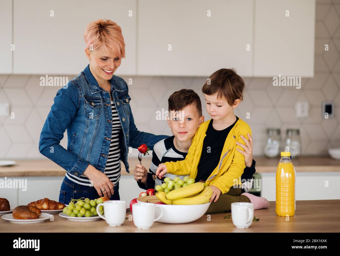 Une jeune femme avec deux enfants de manger des fruits dans une cuisine. Banque D'Images