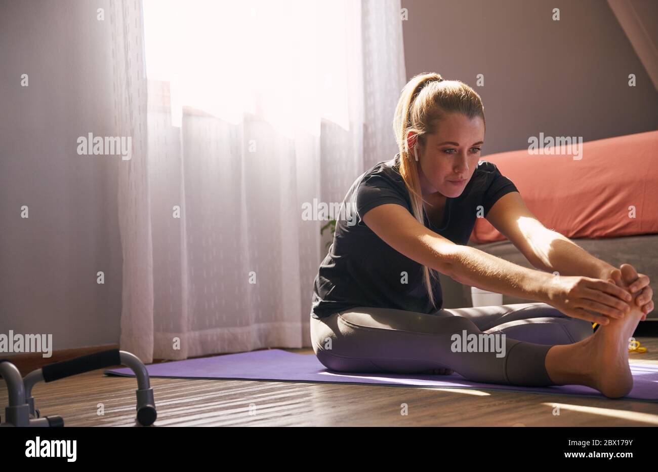 Jeune femme s'étirant sur un tapis de yoga à la maison avec un casque sans fil. Banque D'Images