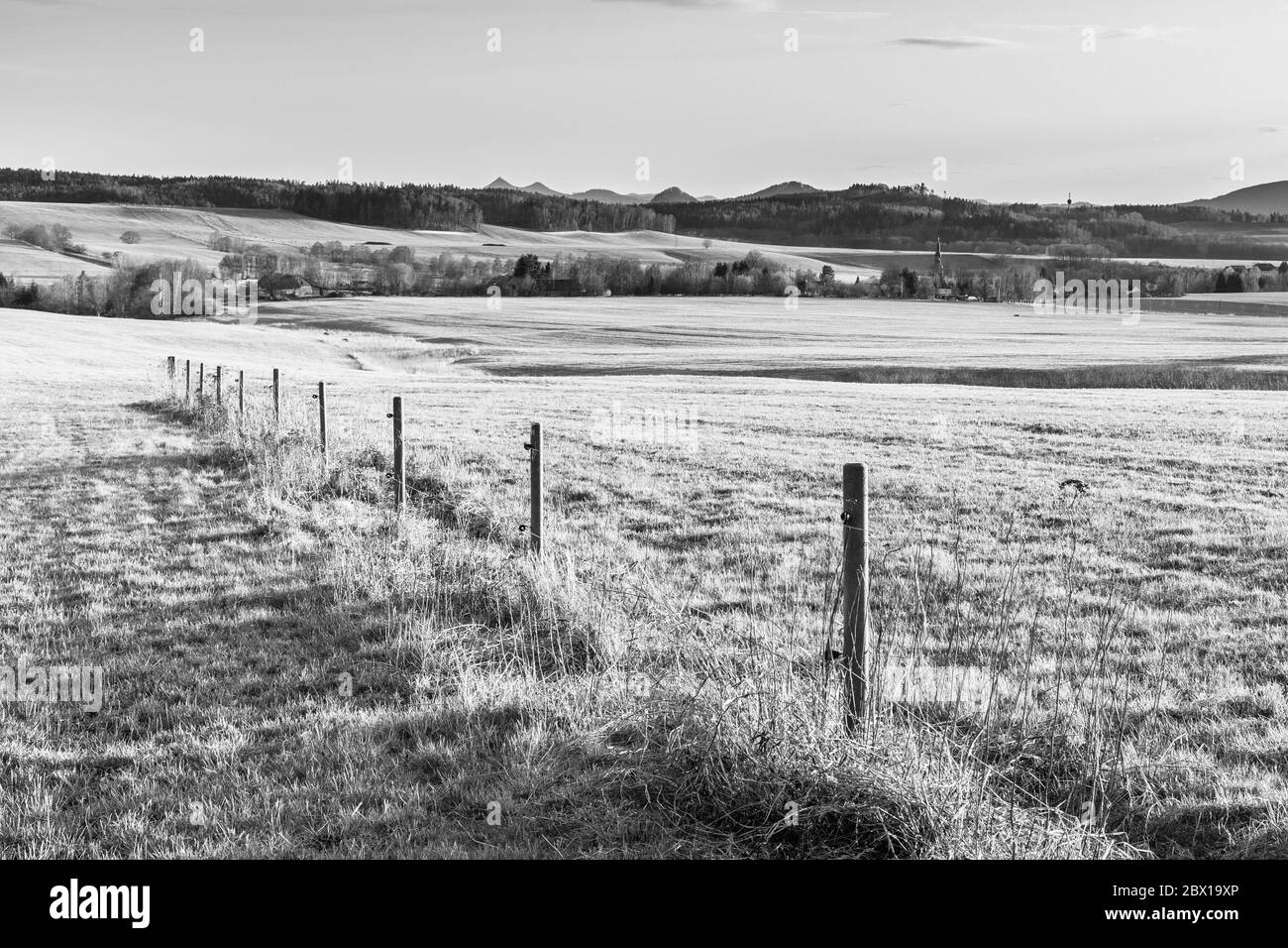 Paysage vallonné éclairé par le coucher du soleil. Champs d'herbe verte et collines sur l'horizont. Campagne rurale de printemps. Ralsko Mountain, République tchèque. Image en noir et blanc. Banque D'Images