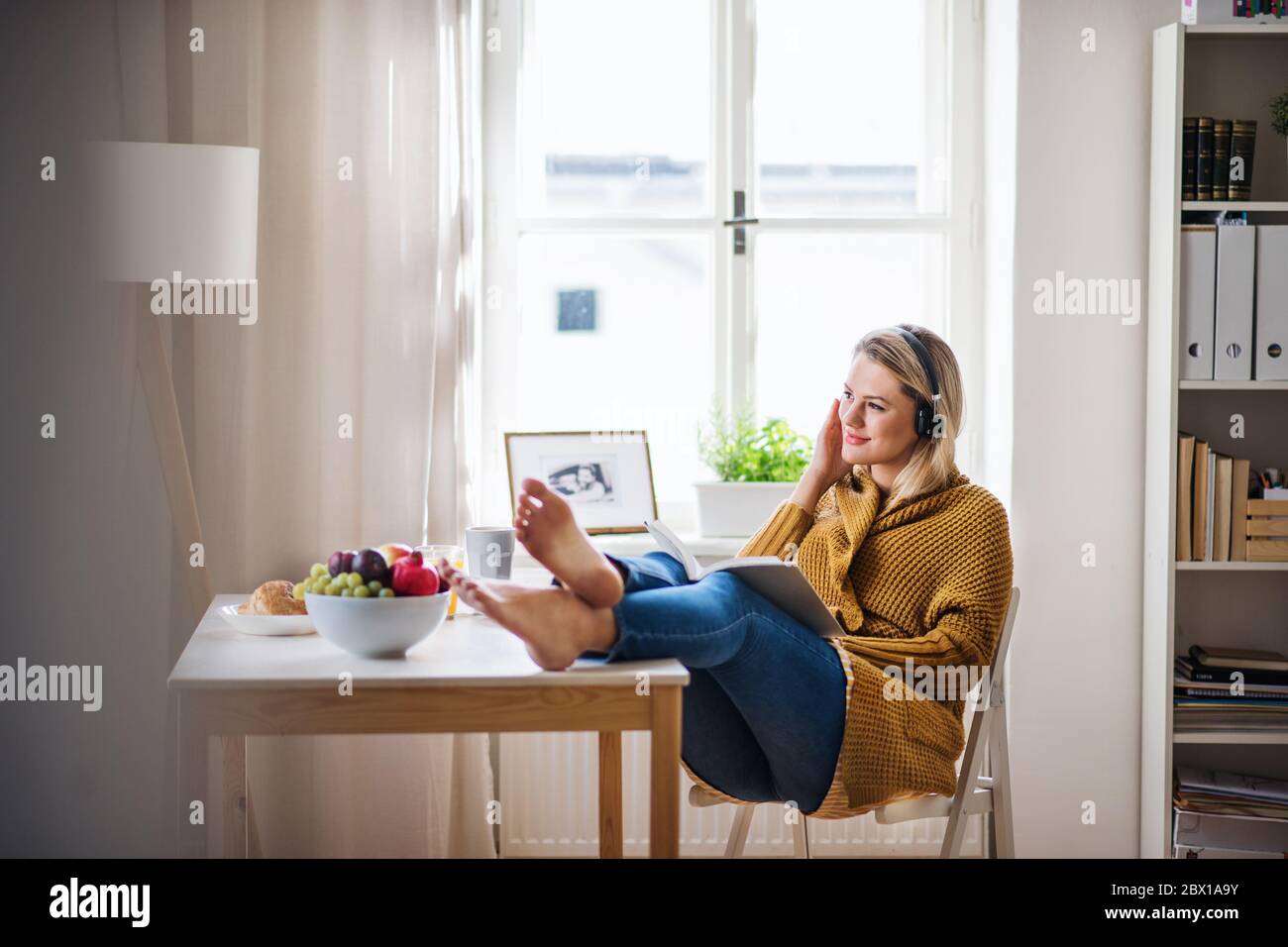 Jeune femme assise à la table à l'intérieur à la maison, lisant un livre. Banque D'Images