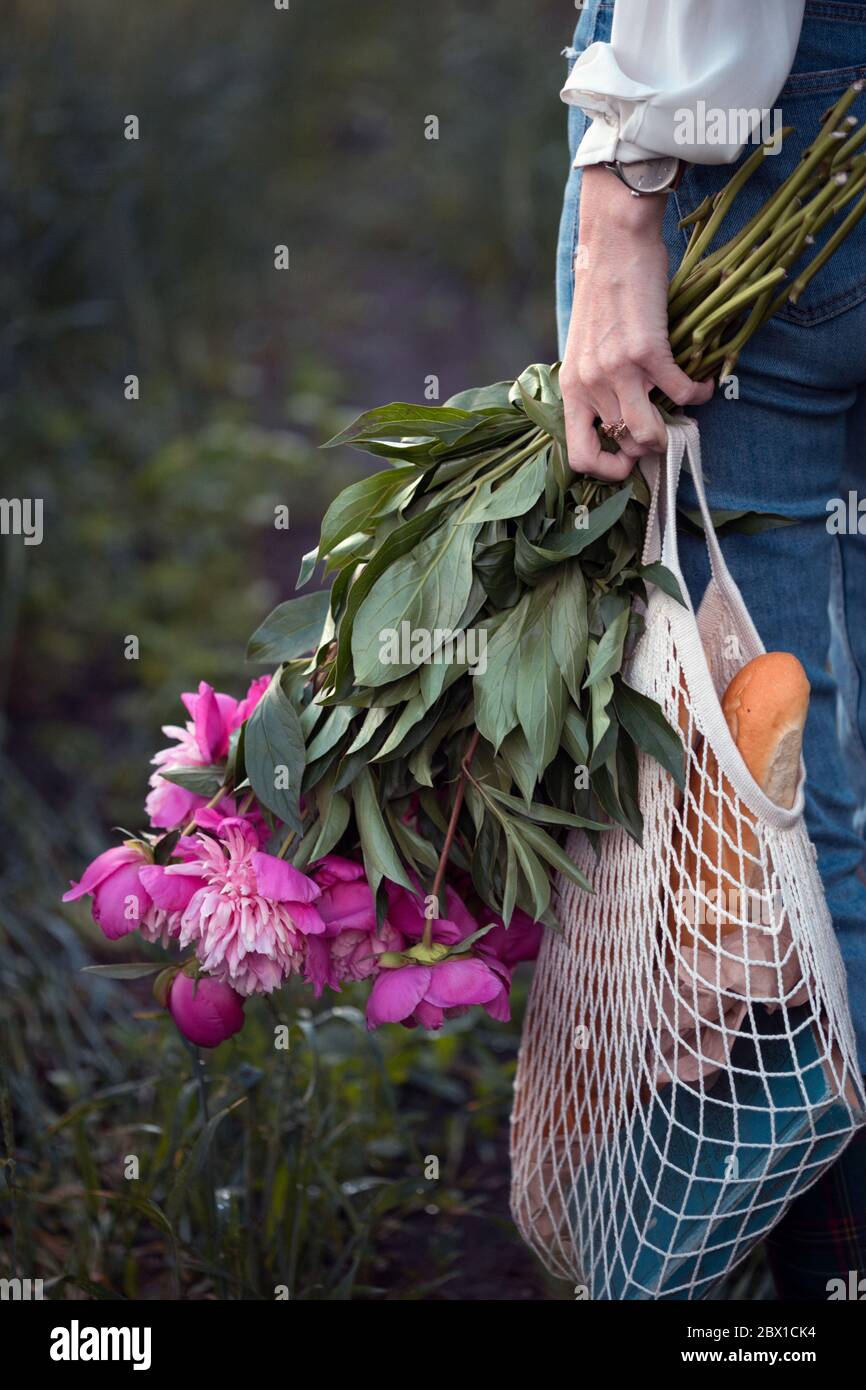 fille avec un bouquet de pivoine et un sac à cordes avec baguettes. ambiance printanière et encore la vie dans le village. Banque D'Images