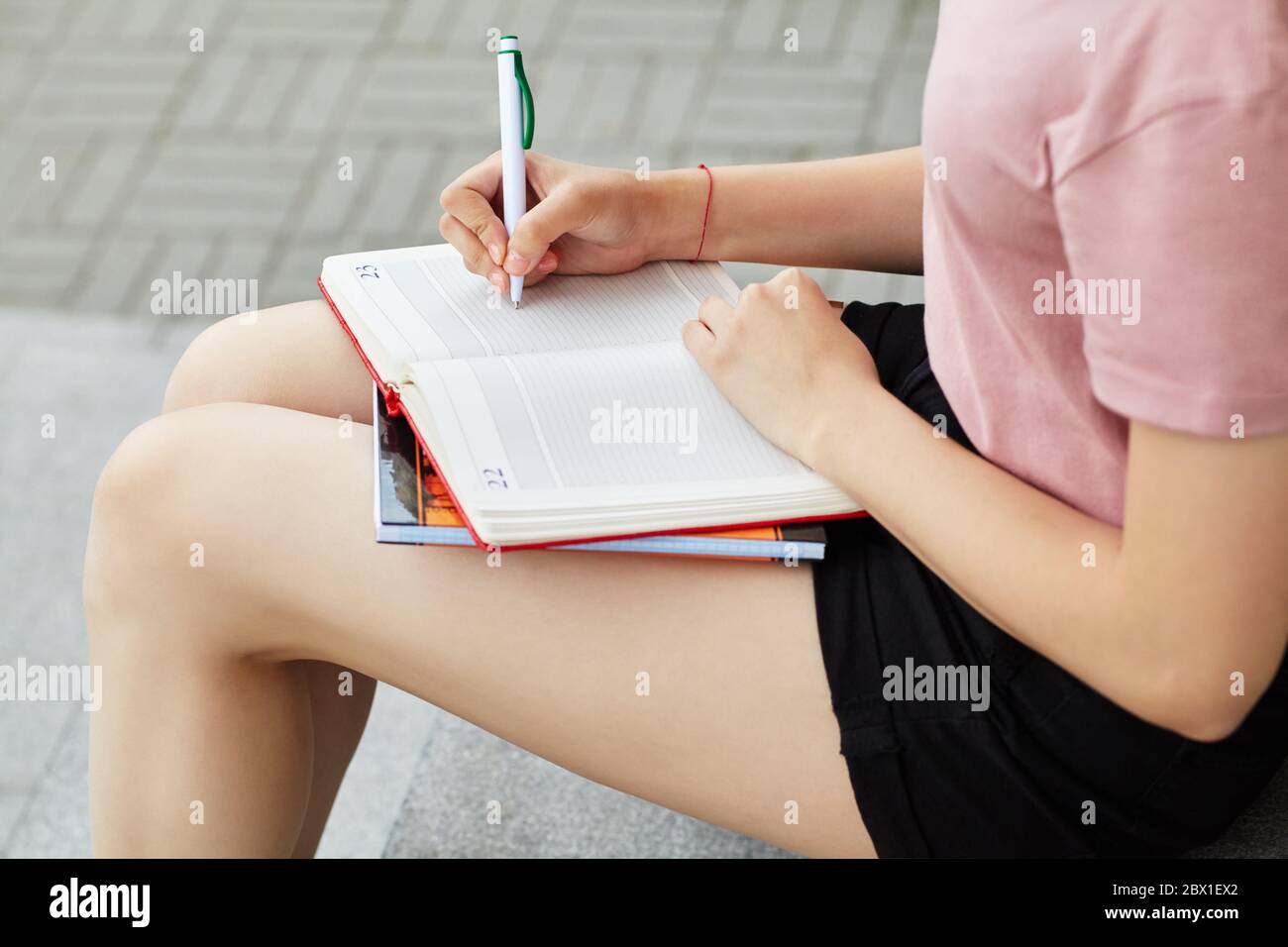Stylo d'écriture fille dans le carnet sur les genoux. Étudiant près de l'université. Banque D'Images
