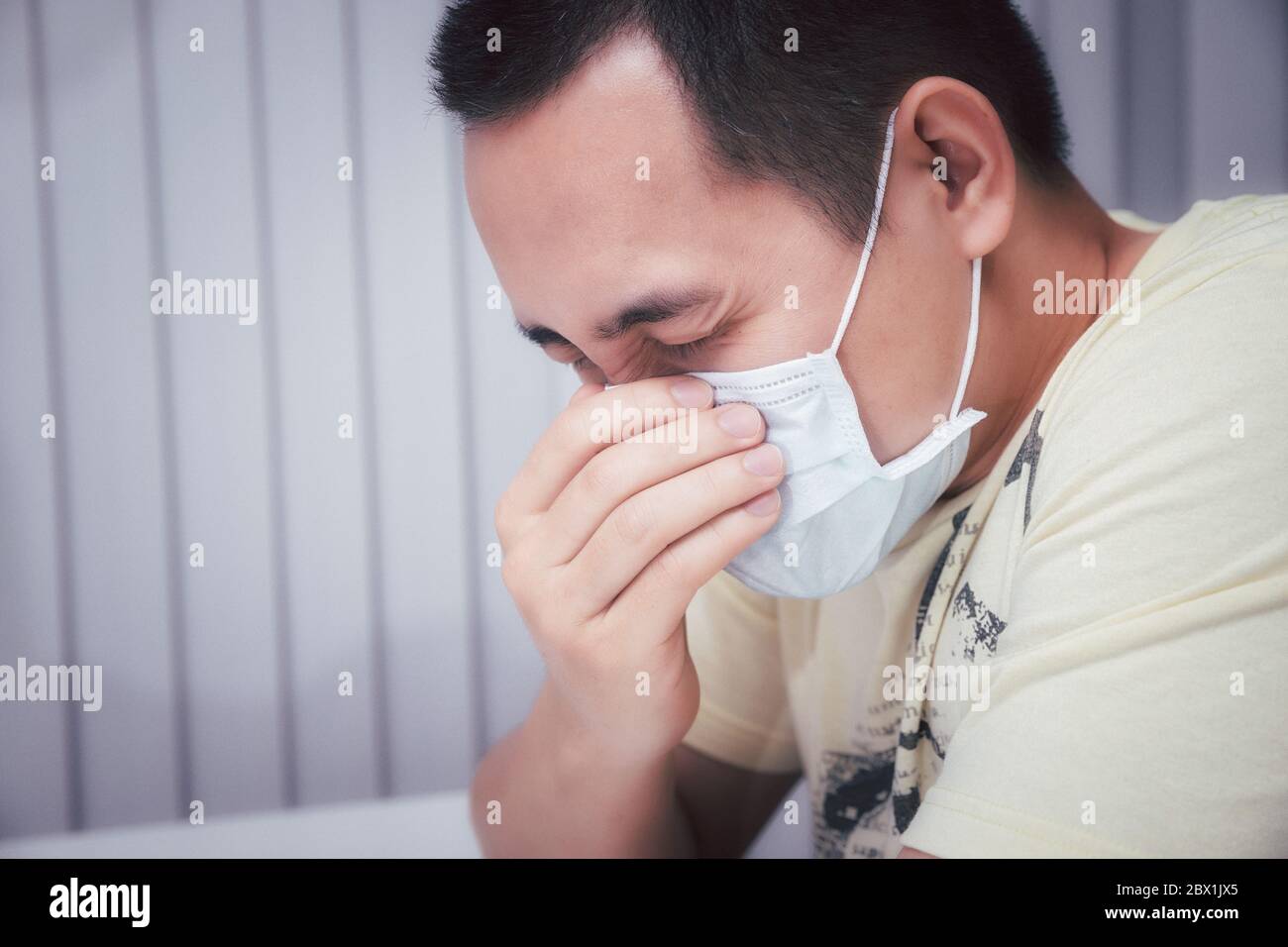 Un homme qui éternue dans un masque protecteur contre les maladies infectieuses transmissibles et comme protection contre la grippe en public. Coronavirus/covid- pandémique Banque D'Images