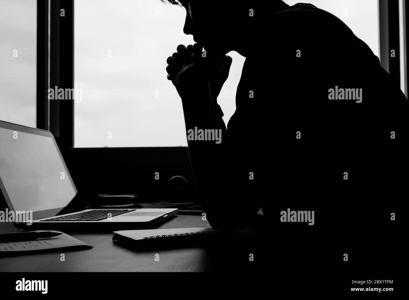 La silhouette d'une image d'un homme regardant son ordinateur portable sur le bureau. Banque D'Images