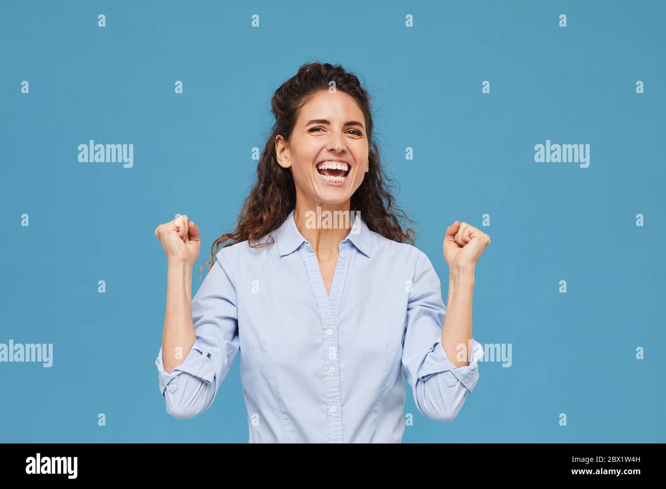 Portrait de la jeune femme avec des cheveux bouclés est heureux de quelque chose en se tenant contre le fond bleu Banque D'Images