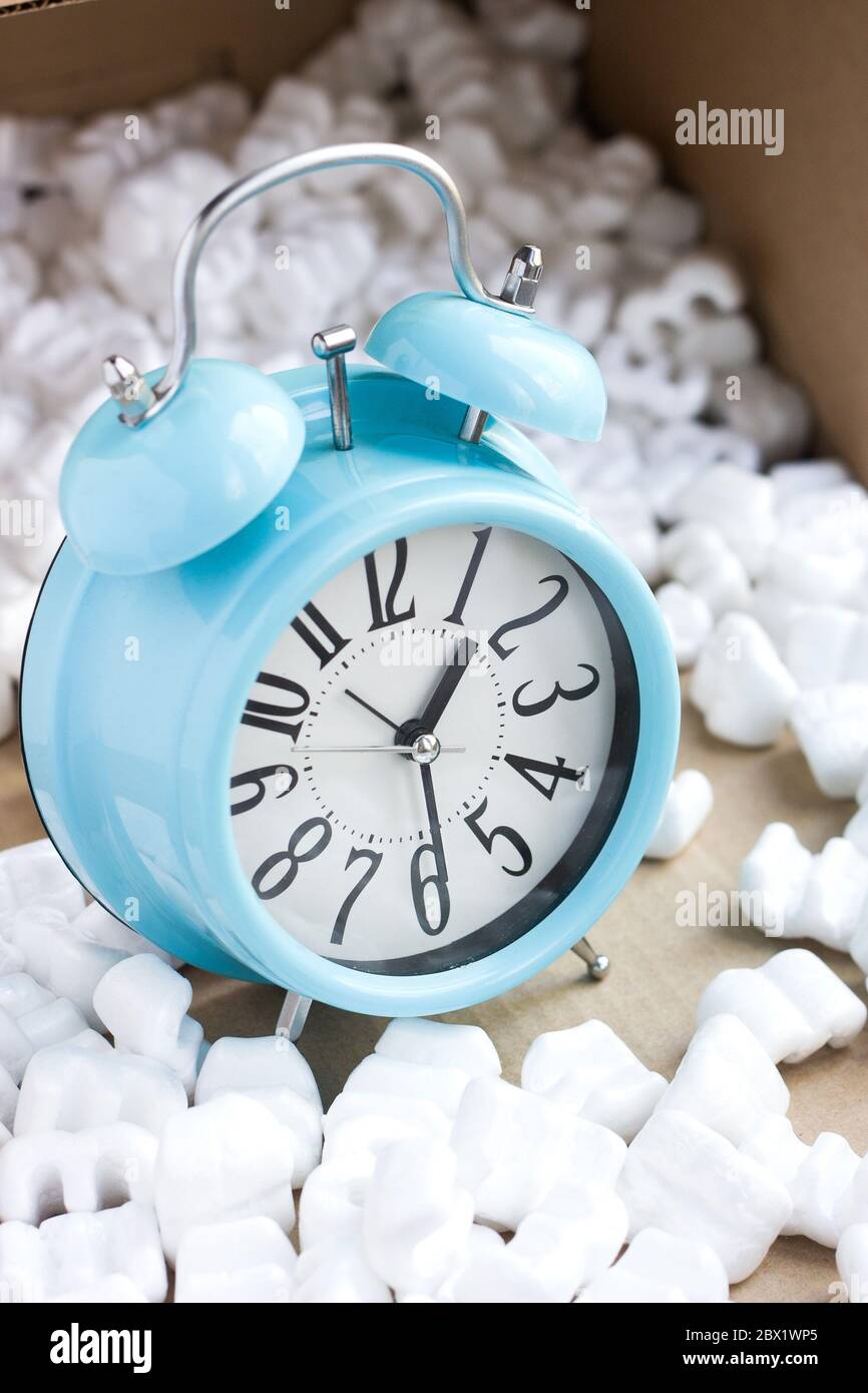Livraison à temps avec prudence. Horloge bleue contre boîte de cartes avec mousse de polystyrène blanche Banque D'Images