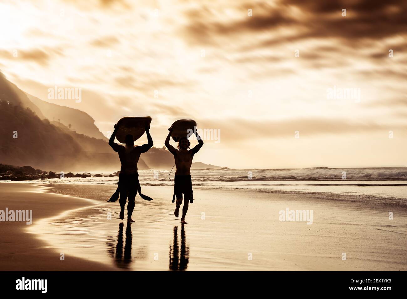 Des amis heureux qui couruent et tiennent des planches de surf sur la plage au coucher du soleil - le père et le fils de surfers faisant de l'exercice d'échauffement Banque D'Images