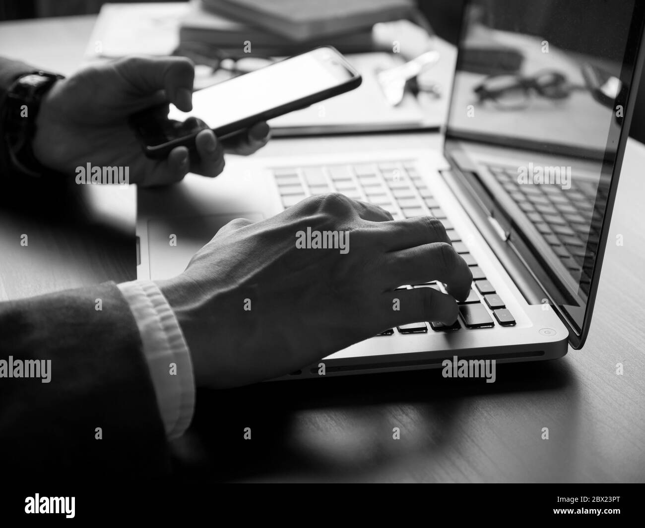 Gros plan sur un homme d'affaires utilisant un ordinateur portable et un smartphone sur le bureau. Noir et blanc Banque D'Images