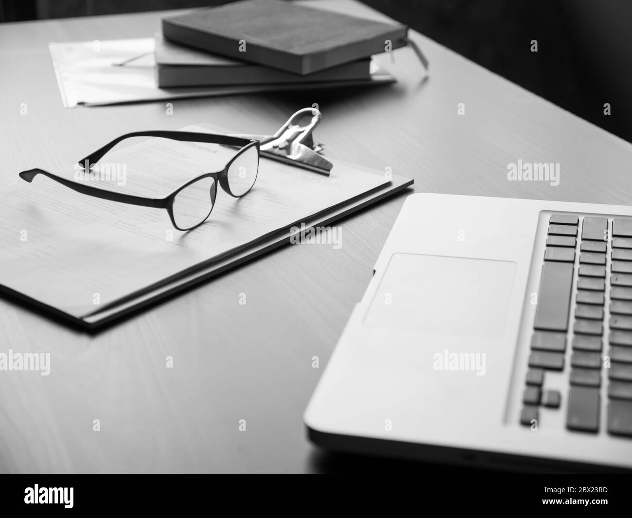 Bureau avec ordinateur portable, lunettes, documents et livres. Noir et blanc Banque D'Images