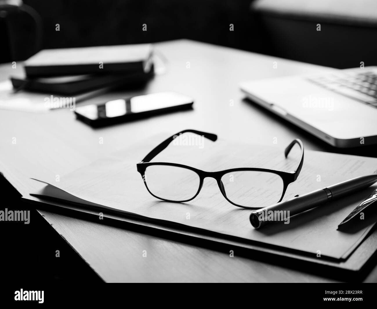 Bureau avec lunettes, documents, ordinateur portable, smartphone et ordinateur portable. Noir et blanc Banque D'Images