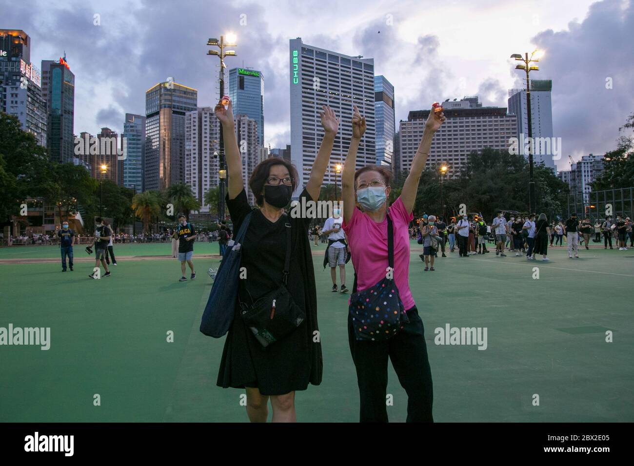 Deux jeunes femmes portant un masque facial lèvent la main comme un panneau indiquant « 5 exige non sur moins ». Des milliers de Hong Kong défient l'interdiction de rassemblement public imposée par le gouvernement à la suite de la crise du coronavirus (COVID-19) et se rassemblent au parc Victoria pour l'anniversaire de Tiananmen. Banque D'Images