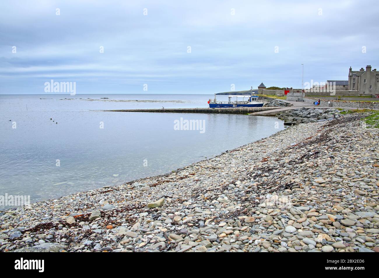 Côte avec galets et rochers et jetée de Sandsayre par une journée d'été grise, Sandwick, îles Shetland, Écosse. Banque D'Images