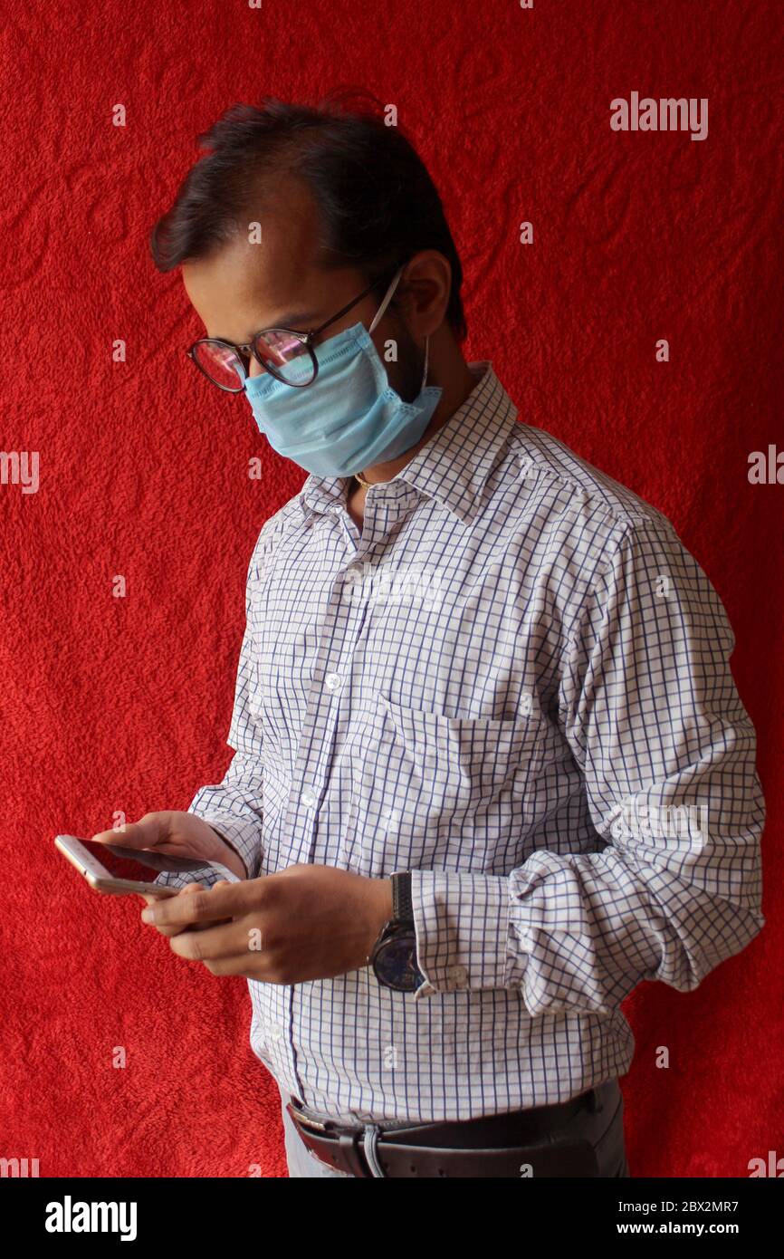 homme adulte barbu utilisant un smartphone tout en portant un masque chirurgical sur fond rouge. Santé, épidémies, médias sociaux, communication et photos de style de vie Banque D'Images