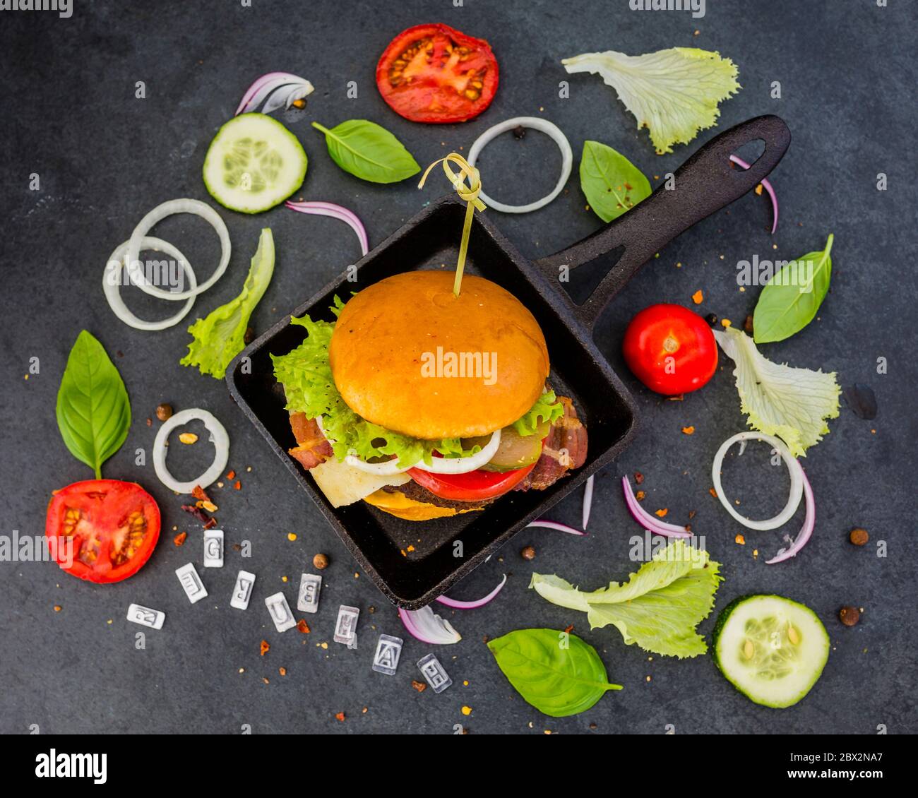 Savoureux hamburger de bœuf grillé dans un pain court croustillant avec laitue et légumes frais sur fond noir de pierre. Banque D'Images