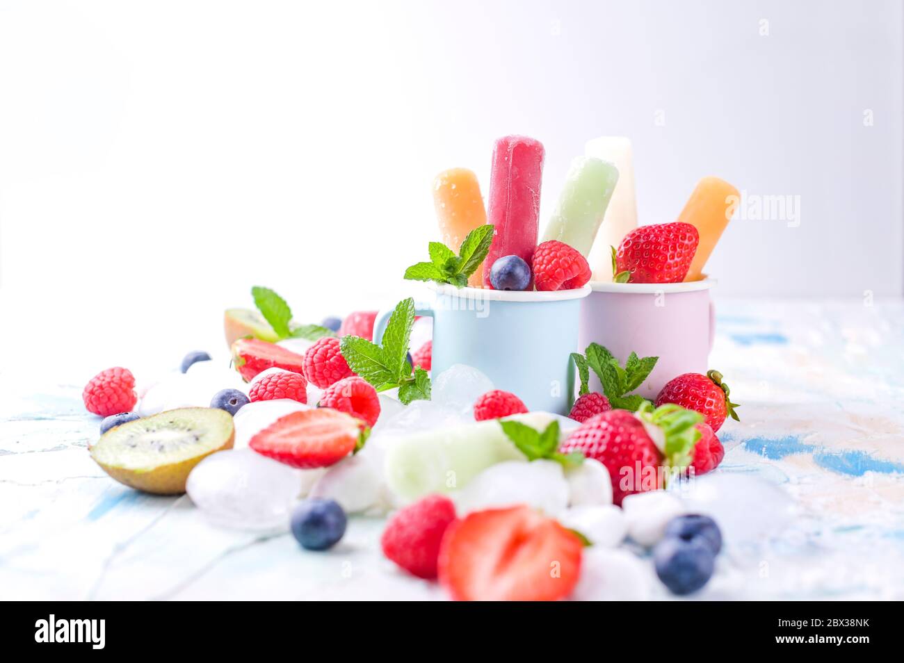 Des papoles de fruits entiers et sains avec des fraises Berries Kiwi sur fond clair, avec un décor de glace, de menthe. Une délicieuse glace aux fruits dans le mug. Espace de copie. Banque D'Images