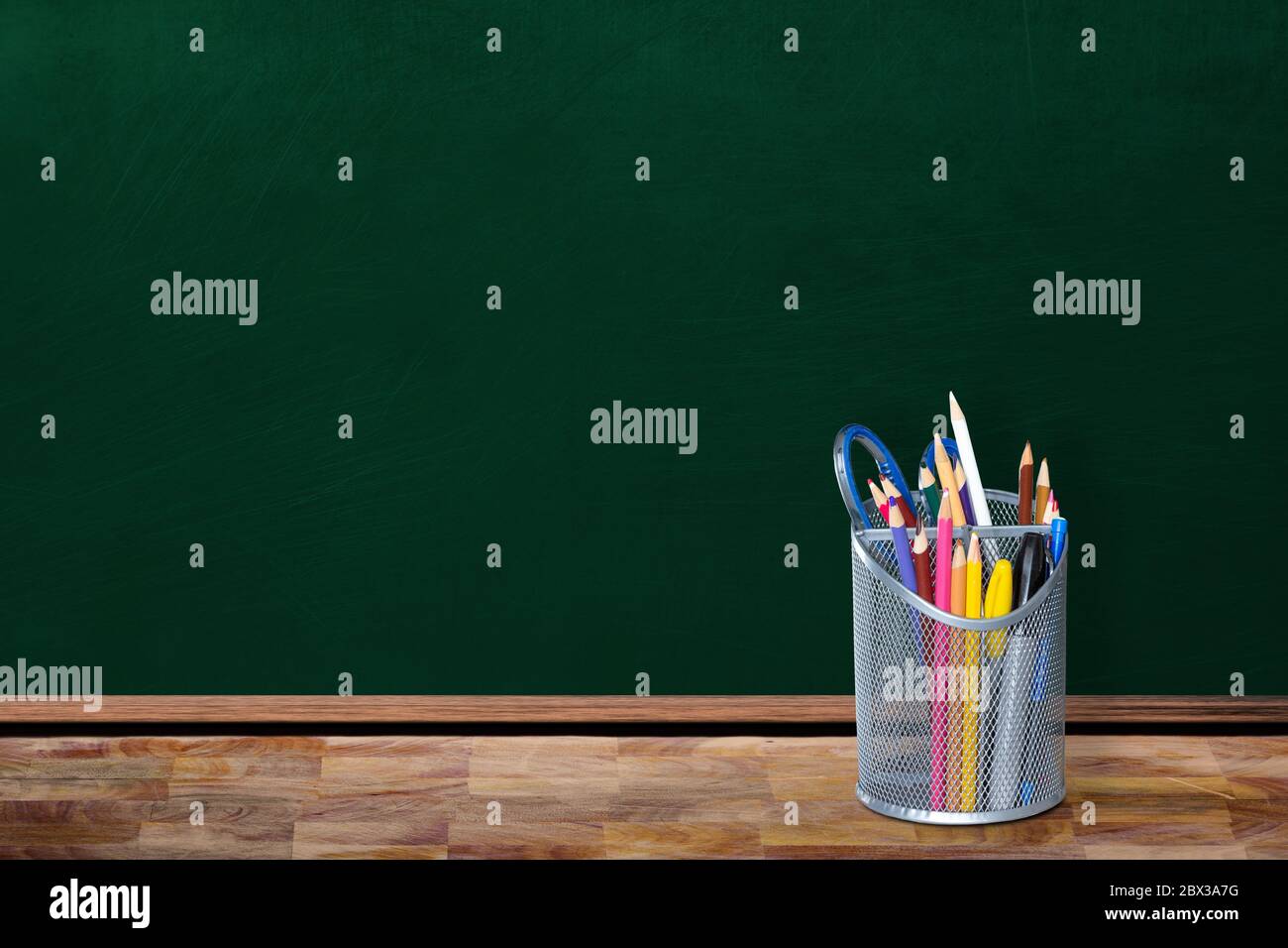 Concept de rentrée scolaire dans un environnement de classe vide avec porte-crayons et agrafs sur table avec espace pour les copies sur tableau noir. Banque D'Images