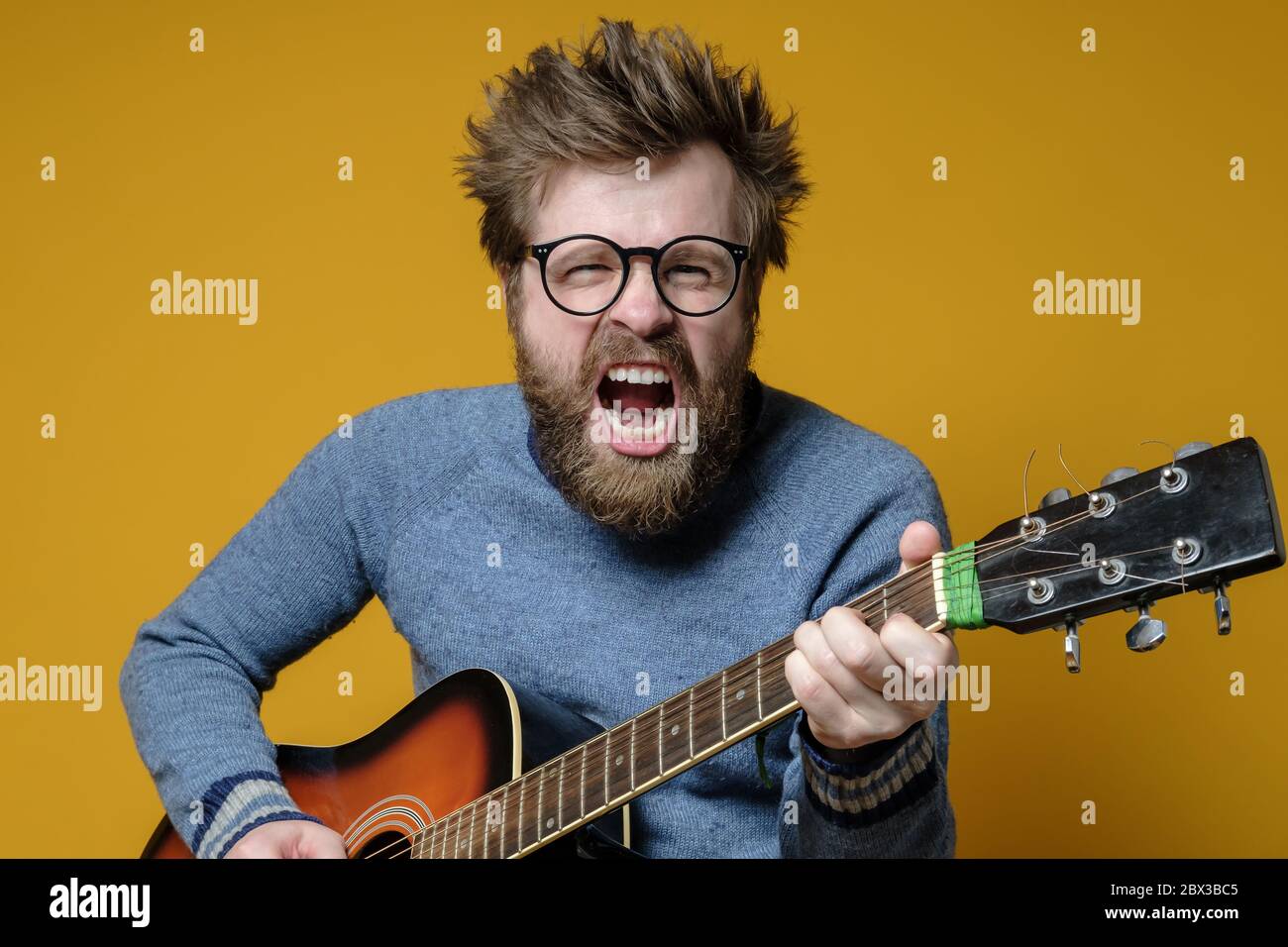 Drôle de hipster dans un ancien chandail joue une guitare acoustique et  chante fort, sur fond jaune. Passe-temps, style de vie Photo Stock - Alamy