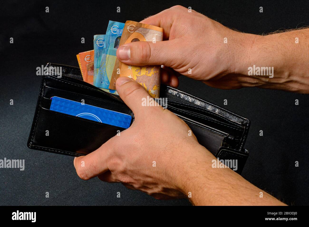 Main de l'homme tirant de l'argent du portefeuille, fond noir et portefeuille noir.2020 Banque D'Images