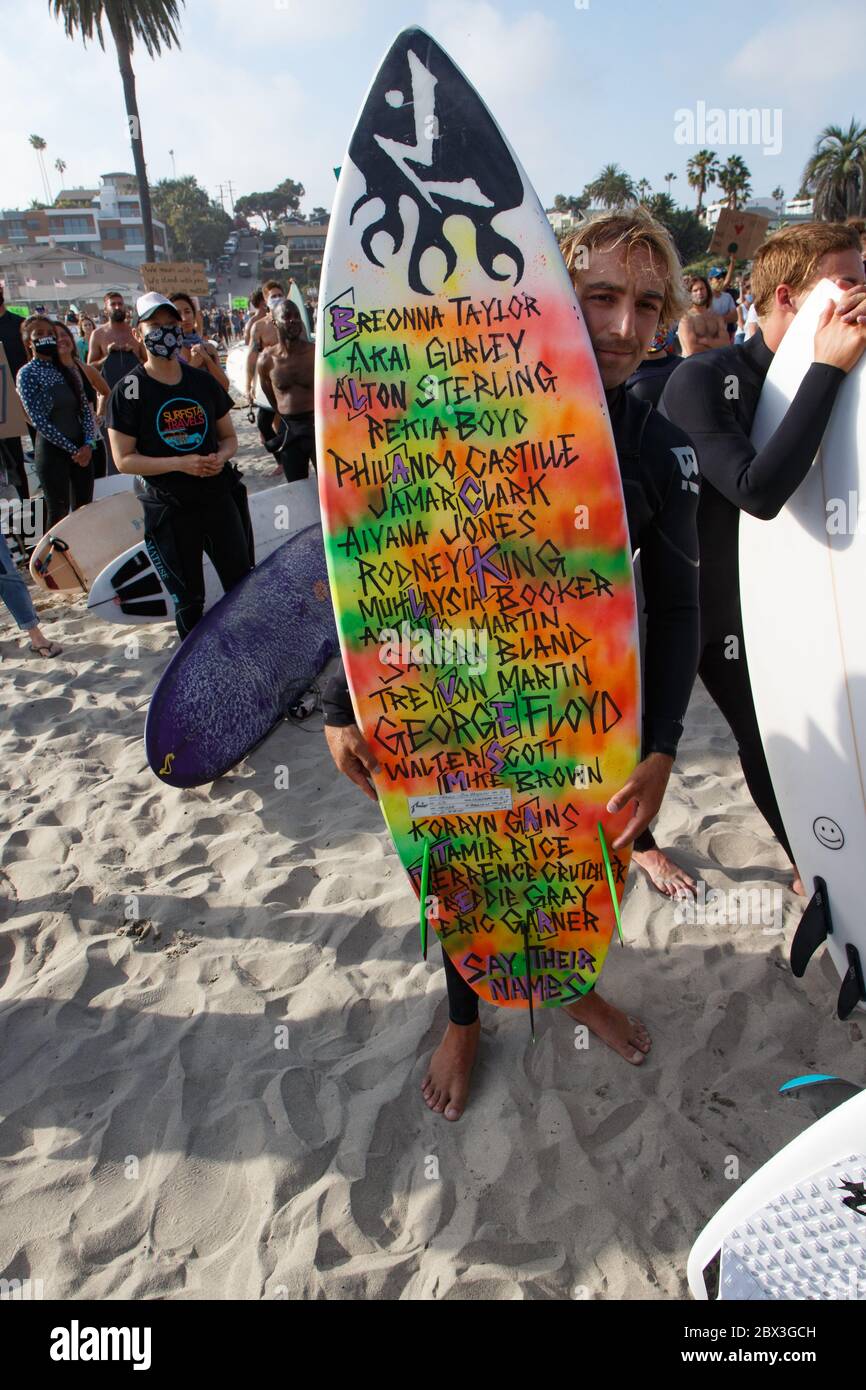 Surfeur Jacob Szekely avec les noms des Noirs américains assassinés sur son surf à la manifestation de Paddle Out for Unity à Encinitas, CA. Banque D'Images