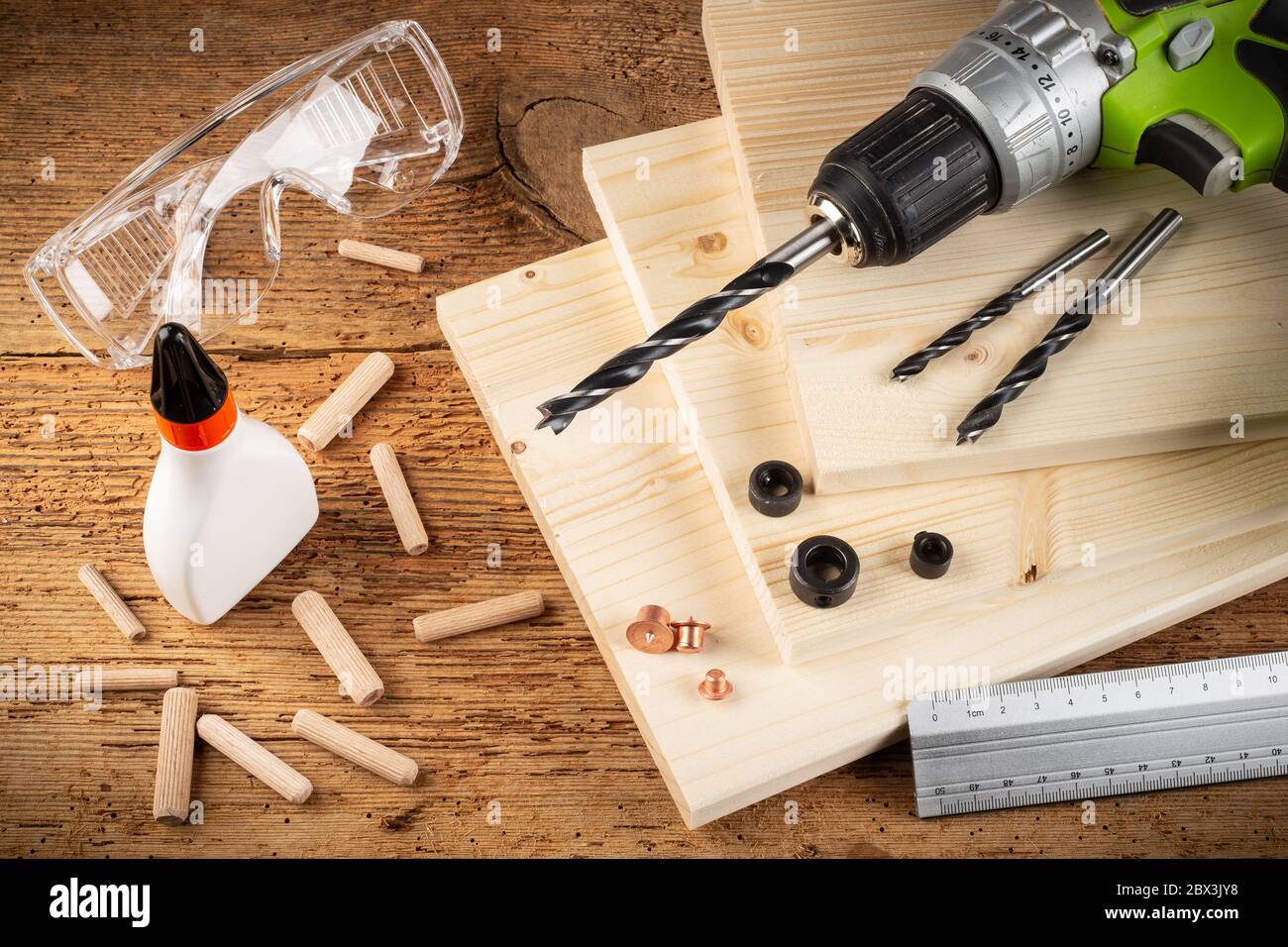 goupilles de cheville en bois tiges de perçage colle bois planches lunettes de sécurité tournevis sans fil et outils sur fond de chêne rustique. Menuisier industrie de la funiture mak Banque D'Images