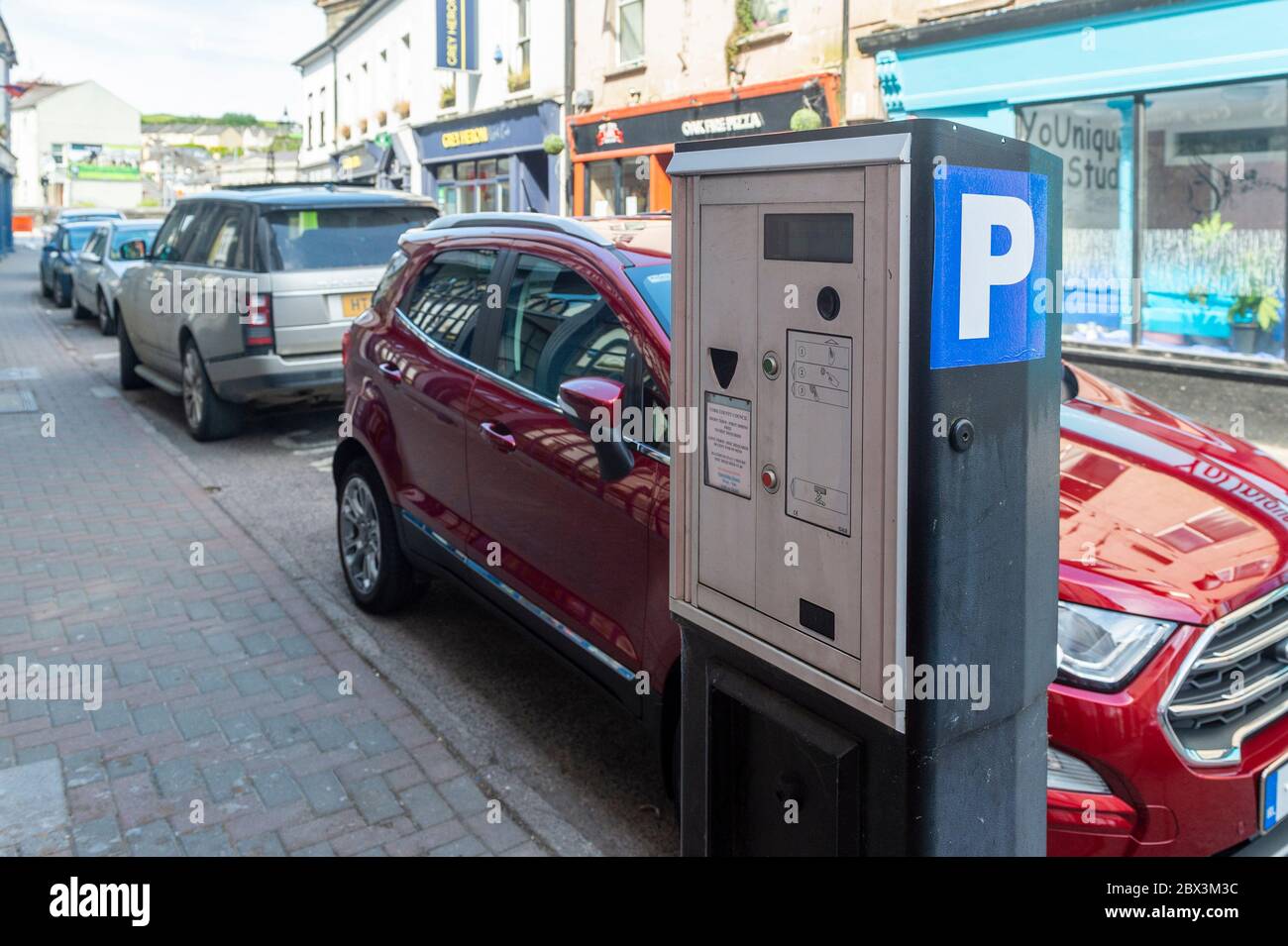Voitures garées dans la rue à côté d'un compteur de stationnement à pièces à Bandon, West Cork, Irlande. Banque D'Images