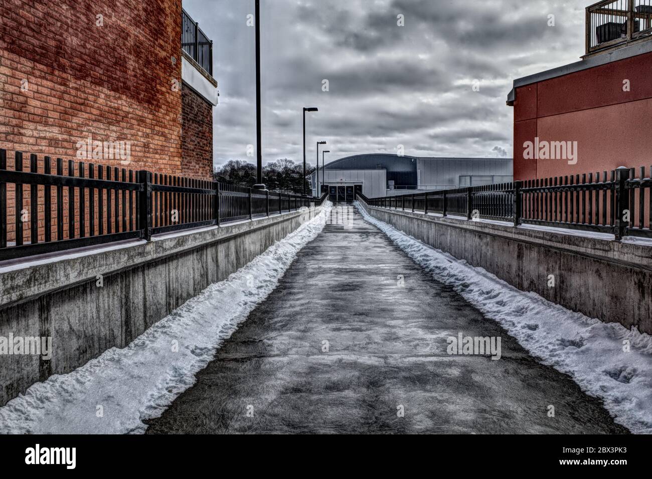Photo High Dynamic Range avec des nuages spectaculaires et une longue allée d'asphalte enneigée entre des bâtiments en briques menant à une nouvelle entrée du centre des congrès Banque D'Images