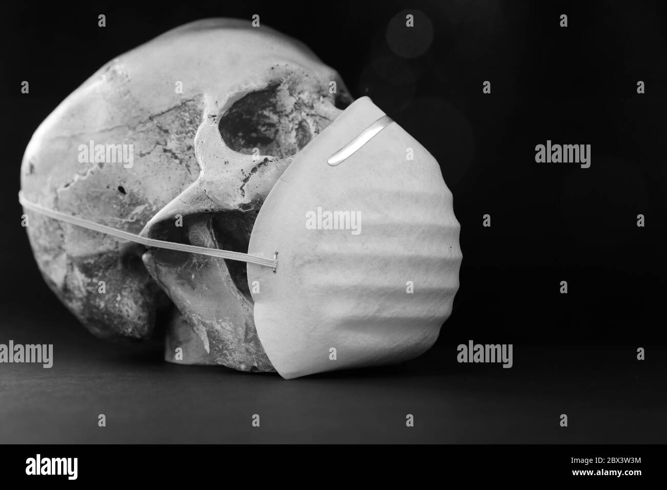 Noir et blanc crâne isolé sur fond noir portant un simple masque en papier pour la protection contre les vapeurs d'odeurs ou les virus. Covid-19 CO Banque D'Images