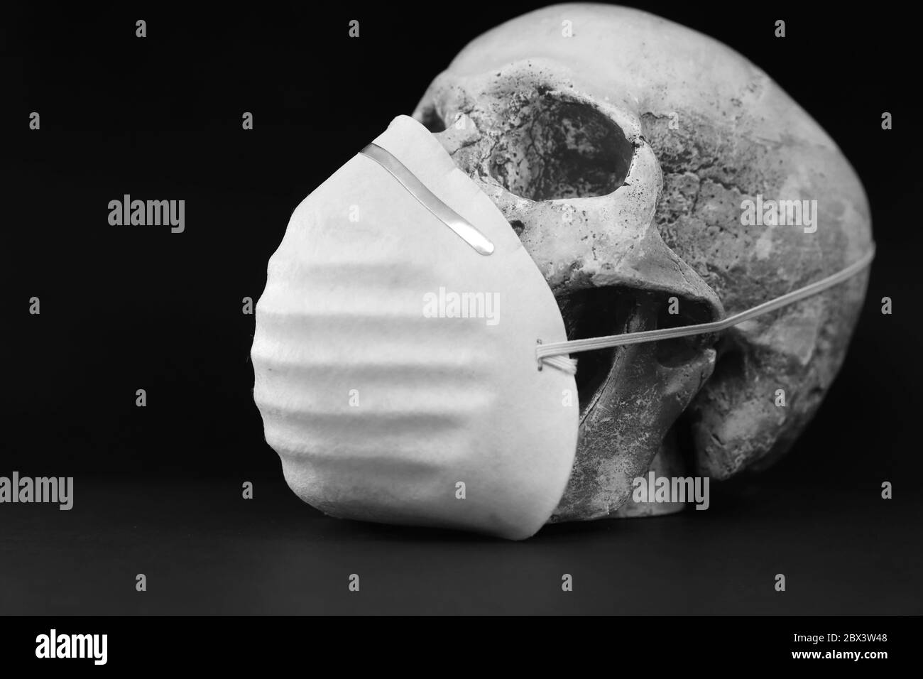 Noir et blanc crâne isolé sur fond noir portant un simple masque en papier pour la protection contre les vapeurs d'odeurs ou les virus. Covid-19 CO Banque D'Images