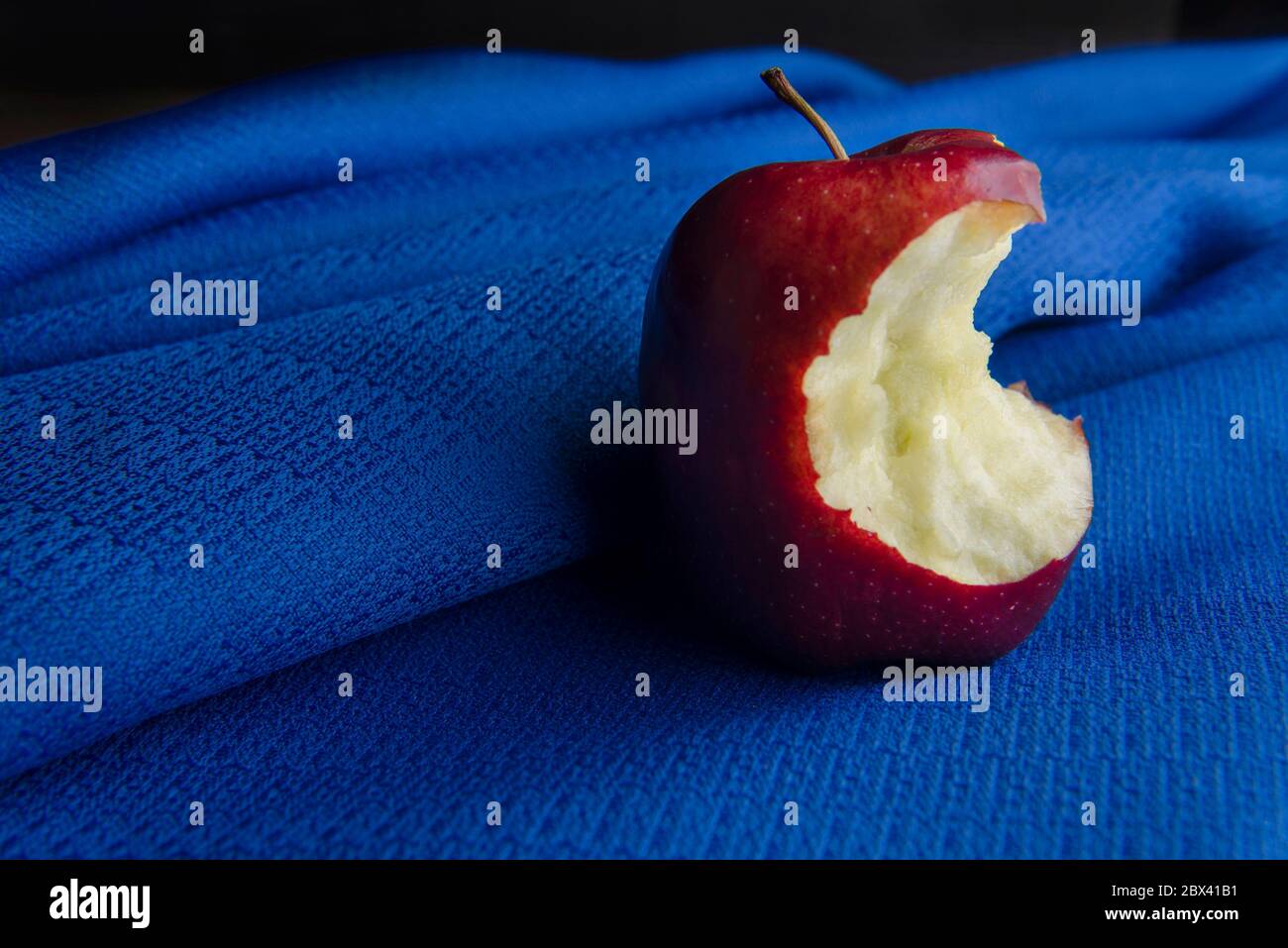 photographie de nourriture sombre ou claire à faible touche. mordiez la pomme rouge sur une nappe bleue. Encore la vie Banque D'Images