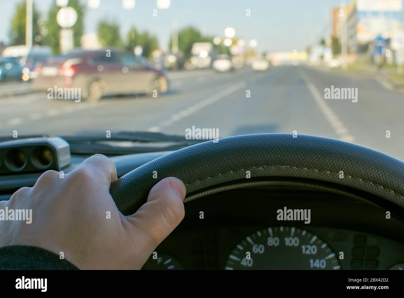 vue de la main du conducteur sur le volant d'une voiture sur le fond d'une route de la ville et d'une voiture quittant la route secondaire sur la route principale Banque D'Images