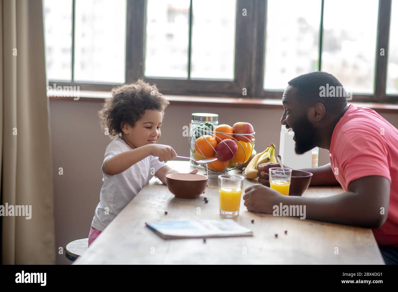 Homme afro-américain dans une chemise rose divertissant sa fille pendant qu'elle mange Banque D'Images