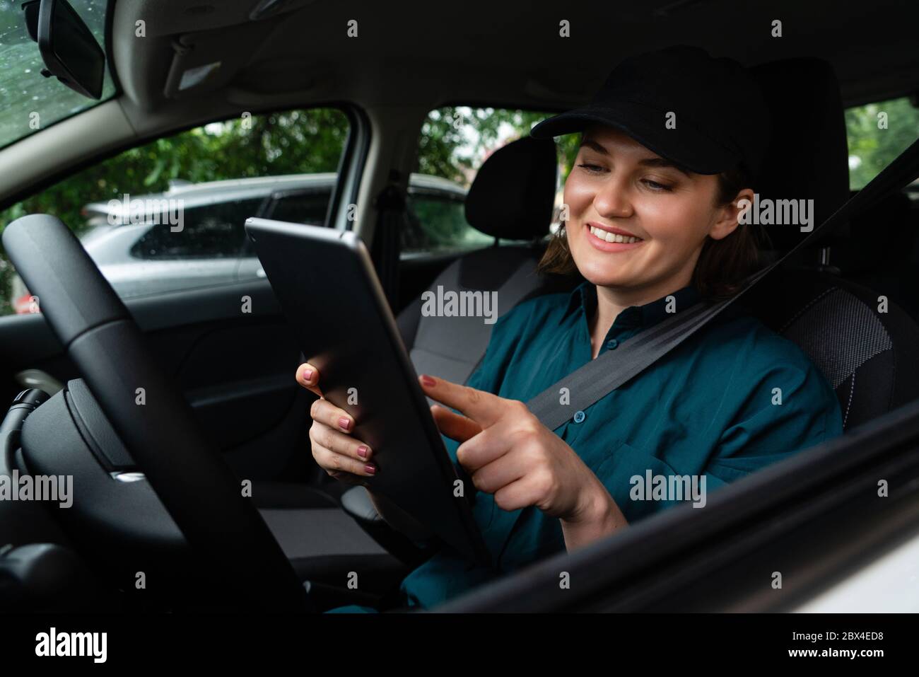 Femme courier assise dans une voiture et regardant une tablette numérique Banque D'Images