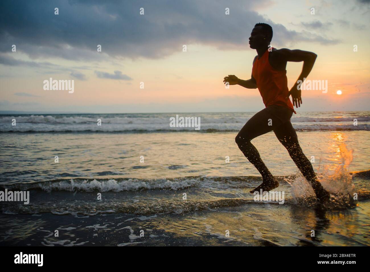 silhouette de jeune sportif et de la forme afro-américain homme de sport faisant l'entraînement de course au coucher du soleil à la plage entraînement dur de jogging pieds nus dans la santé Banque D'Images