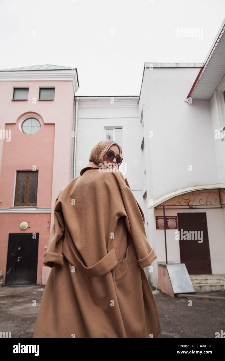 Jeune femme élégante portant un manteau chaud beige, un pantalon et des  lunettes de soleil marchant dans la rue de la ville en saison froide. Hiver  mode, look élégant, tenue Photo Stock -