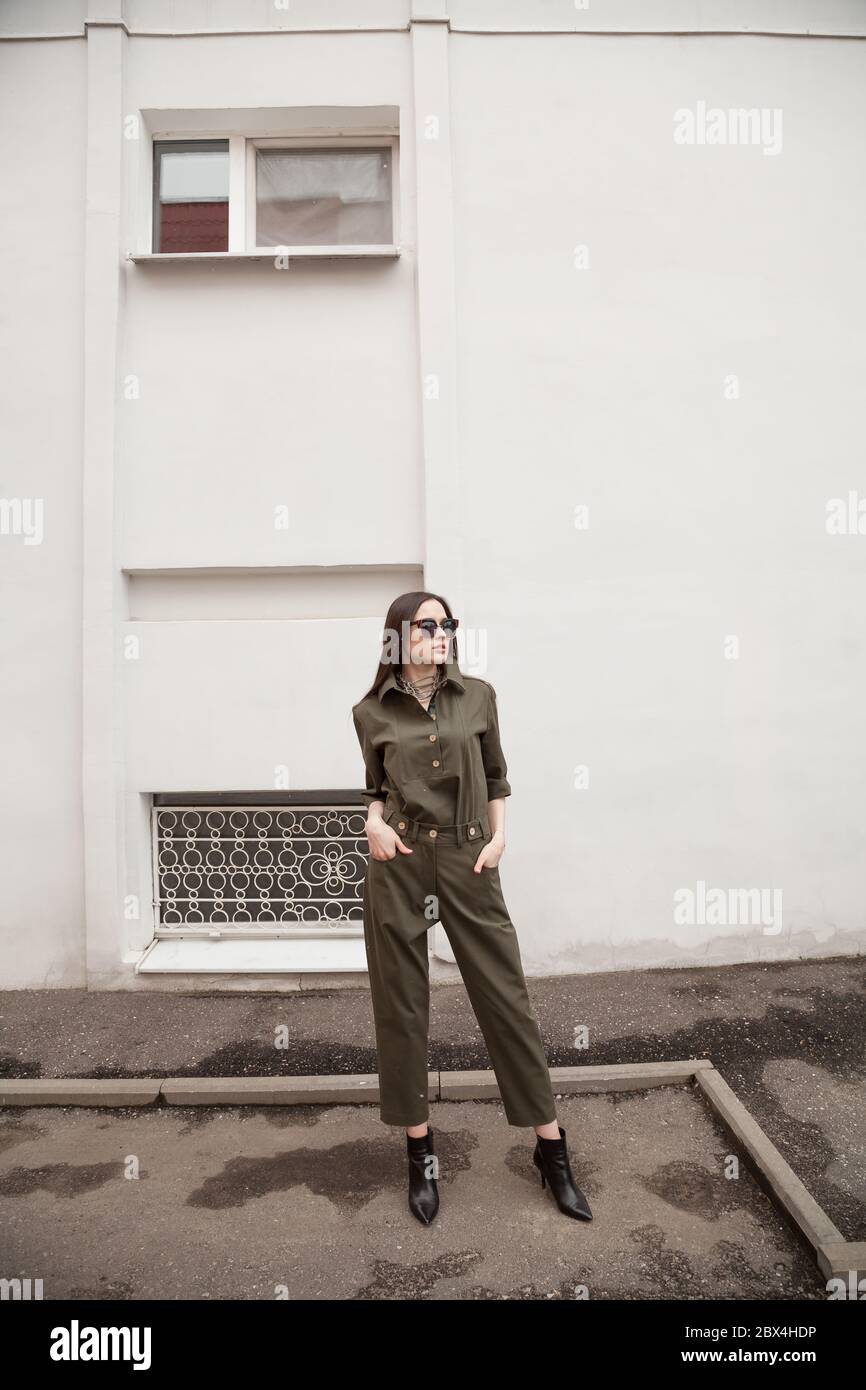 élégante et belle jeune femme dans un costume vert tendance avec des lunettes de soleil posant dans la rue dans l'environnement urbain. Style professionnel tendance Banque D'Images