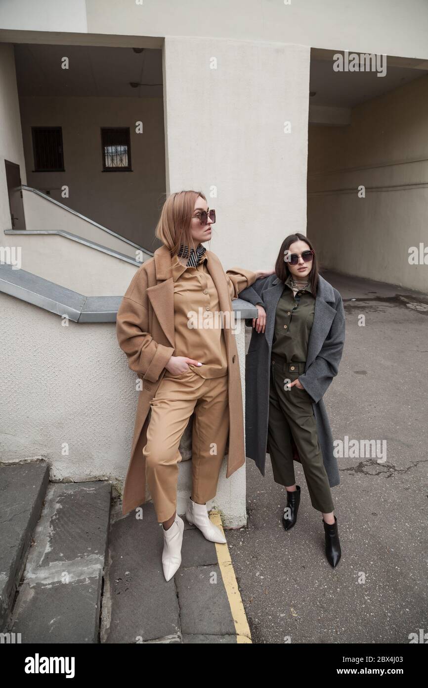 Deux amies portant une tenue urbaine tendance, des manteaux en laine et des bottes avec talons. De jeunes amis attendent dans les escaliers pour leur petit ami Banque D'Images