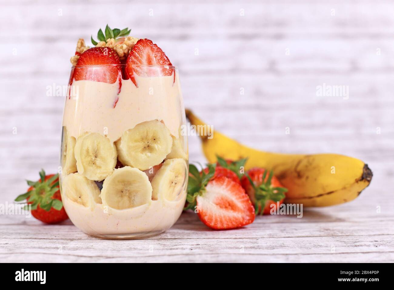 Dessert d'été sain aux fruits de banane et de fraise avec yaourt et layette en verre de granola entourée d'ingrédients frais Banque D'Images